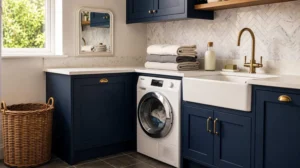 Modern laundry room renovation featuring navy blue shaker cabinets, white farmhouse utility sink, brass faucet, marble herringbone backsplash, quartz countertops, front-load washing machine, and woven laundry basket