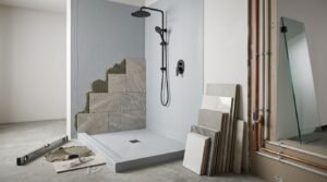 Shower installation in progress featuring a low-profile grey shower tray, partially tiled wall with large marble-look tiles and exposed notched adhesive, matte black dual showerhead, tile spacers, spirit level, and plumbing pipes next to a glass panel.