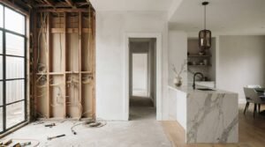 Home renovation showing an unfinished wall with exposed framing and wiring beside a completed modern kitchen with a marble island