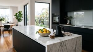 Modern kitchen featuring a white marble waterfall island, matte black cabinetry, and a bowl of fresh lemons