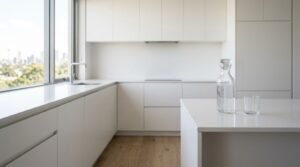 Minimalist white kitchen with sleek cabinetry, a waterfall island, and large windows overlooking the city skyline