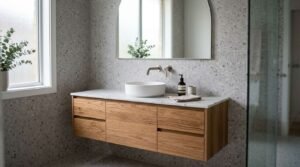 Modern bathroom featuring a floating natural oak vanity with marble countertop, white vessel basin, wall-mounted brushed tapware, arched mirror, and terrazzo tile wall