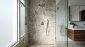 Modern walk-in shower featuring natural stone marble tiles, brushed nickel rain shower head, handheld wand, linear drain, and frameless glass enclosure