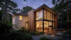 Modern two-storey home extension with floor-to-ceiling glass walls, timber cladding, and landscaped garden at dusk