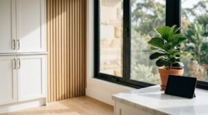 Modern interior featuring decorative wood slat wall paneling, white cabinetry, large black-framed windows, and a marble countertop