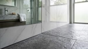 Modern bathroom floor interior with textured dark grey slate tiles, large-format marble wall tiles, and a frameless glass shower enclosure