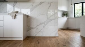 Modern white kitchen island with an integrated Calacatta marble slab partition wall, light-toned hardwood flooring, and seamless flat-panel white cabinetry.