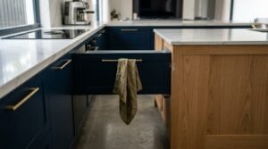 Kitchen layout design flaw showing an open navy blue drawer colliding directly with the side panel of an adjacent oak kitchen island bench, demonstrating insufficient clearance space.