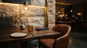Cozy modern restaurant interior with a wooden dining table, leather chair, stone and brick accent wall, and warm ambient lighting