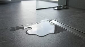 Close-up of a wet room floor showing standing water near a linear drain, highlighting drainage and floor slope considerations.