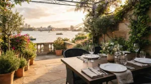 Alfresco restaurant terrace with elegantly set dining table, lush garden, and stunning Sydney Harbour sunset views