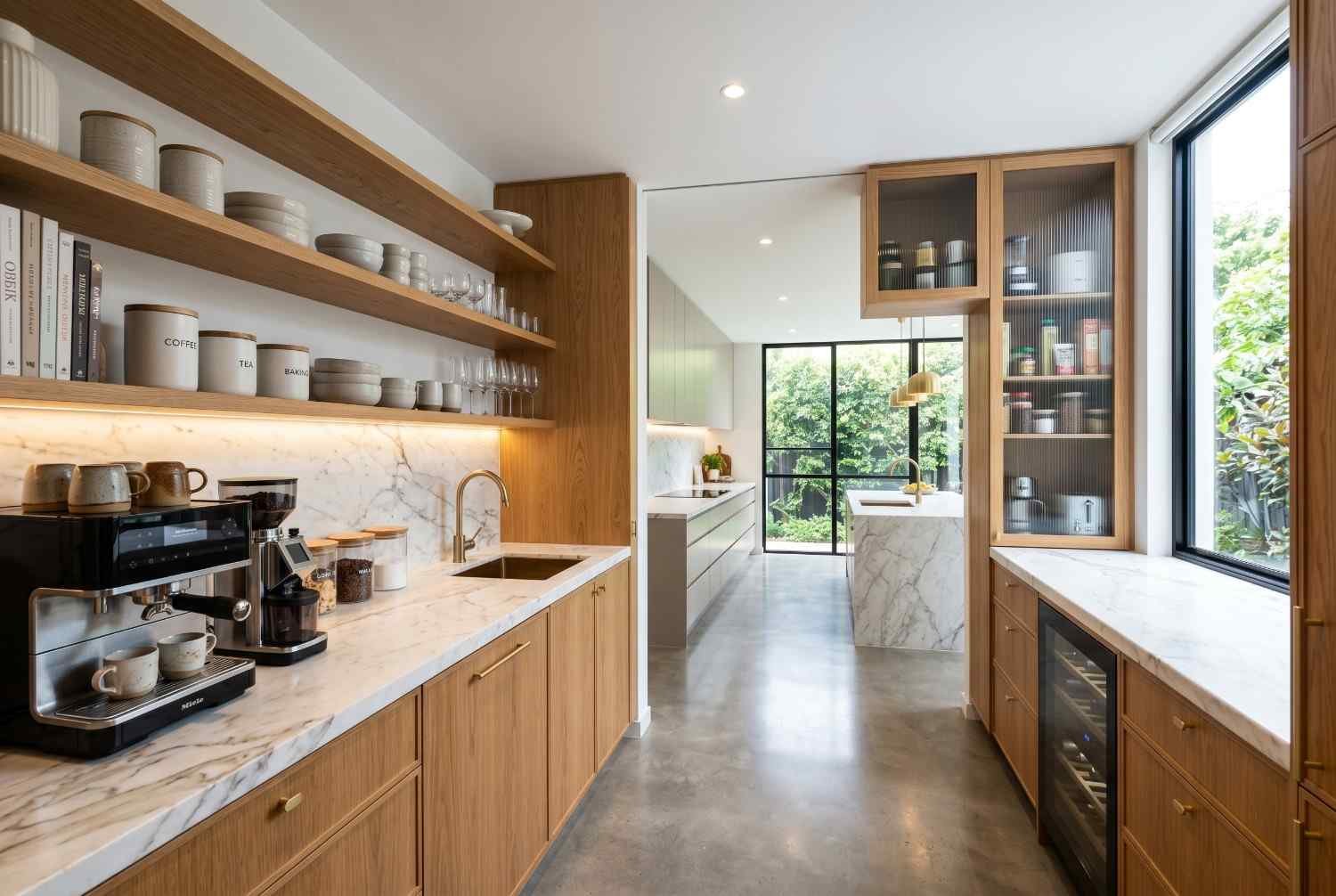 Luxury butler’s pantry with custom timber cabinetry, marble countertops, open shelving, integrated sink, and built-in beverage storage. Modern kitchen pantry design featuring premium finishes, ample storage solutions, and seamless connection to a contemporary open-plan kitchen renovation