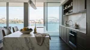 Luxury modern kitchen with a white marble waterfall island featuring floor-to-ceiling windows overlooking the Sydney Opera House and Harbour Bridge