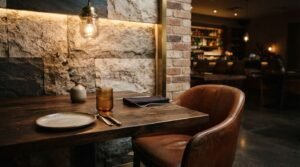 Cozy modern restaurant interior with a wooden dining table, leather chair, stone and brick accent wall, and warm ambient lighting