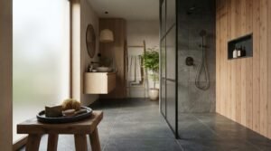 Contemporary Japandi bathroom featuring a walk-in glass shower, warm timber wall panels, floating wood vanity, vessel sink, dark stone tiles, frosted window, and minimalist natural décor.