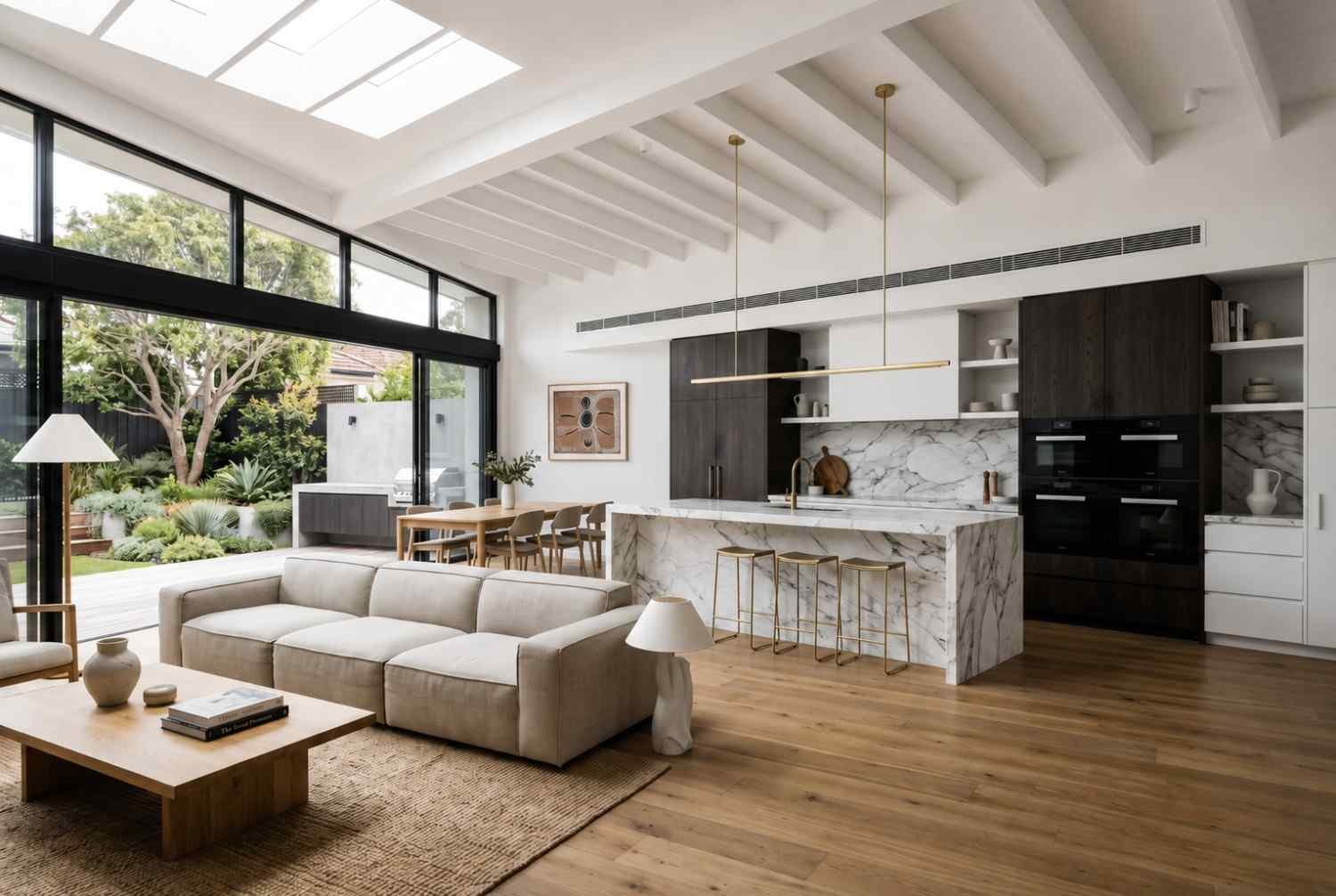 Bright open-plan kitchen and living area with marble island, skylights, and contemporary finishes after renovation.