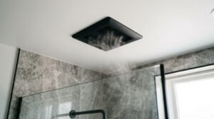Matte black square bathroom ceiling exhaust fan extracting shower steam in a modern bathroom with grey marble wall tiles