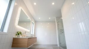 Modern bright bathroom with white vertical stacked tiles, floating oak vanity, round vessel sink, LED illuminated vanity mirror, and glass shower screen