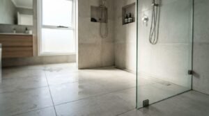 Seamless curbless wet room shower with large-format light grey tiles, frameless glass panel, dual recessed wall niches, and stainless steel linear floor drain