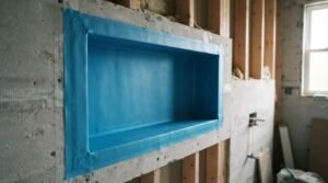 Preformed recessed shower niche installed with blue liquid waterproofing membrane tanking around cement backer board wall studs