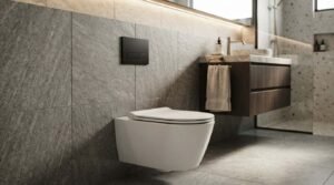 Wall-hung rimless toilet with a matte black dual-flush actuator plate mounted on a textured grey stone tile feature wall beside a floating dark wood vanity