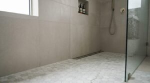 Walk-in shower featuring small marble hexagon floor tiles paired with large-format grey porcelain wall tiles and a linear drain