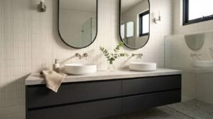 A modern master bathroom featuring a matte black floating double vanity with a light concrete countertop, dual round white vessel sinks, brushed nickel wall-mounted faucets, twin pill-shaped black-framed mirrors, and vertically stacked kit kat mosaic wall tiles
