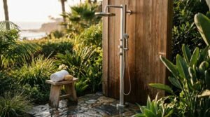 Freestanding brushed stainless steel outdoor shower tower mounted on vertical teak wood panel in tropical garden near ocean view