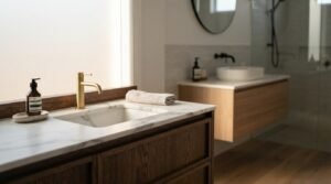 Dark wood bathroom vanity with white marble countertop, undermount sink, and brushed brass faucet in the foreground, with a floating light oak vanity and vessel sink in the background