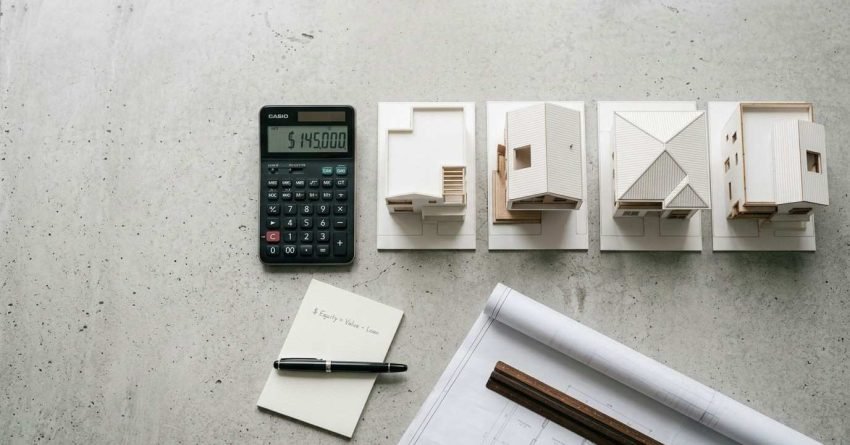 Calculator displaying a renovation budget alongside house design models, blueprints, and planning materials for home renovation cost estimation.