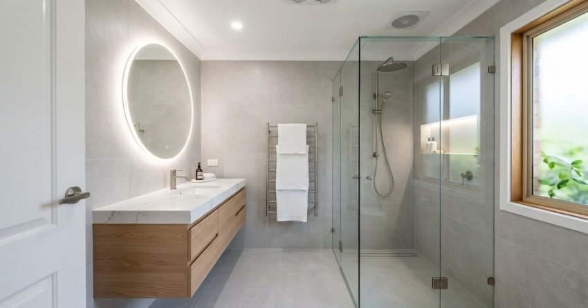 Luxury bathroom renovation featuring a floating timber vanity, illuminated round mirror, frameless glass shower, recessed wall niche, large-format tiles, and a contemporary spa-inspired design.