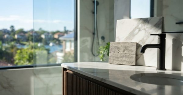 Modern bathroom vanity with a black faucet, stone and marble samples, and a walk-in shower, showcasing bathroom renovation material selections.