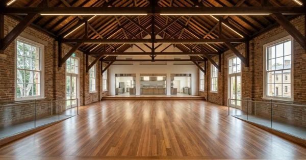 Historic hall renovation featuring exposed timber trusses, restored brick walls, polished hardwood flooring, modern linear lighting, and a spacious multi-purpose event venue interior.