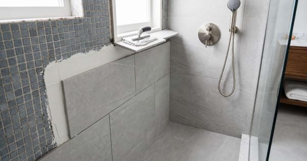 Modern grey porcelain shower tile installation in progress next to blue mosaic wall